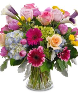 Compact low vase filled to brim with hydrangea, roses, gerbera daisies, calla lilies, and other accent flowers.