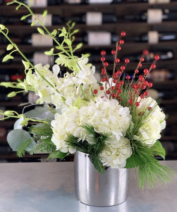 A silver ceramic cylinder filled with accents of white hydrangea, dendrobium orchids, and faux red berries